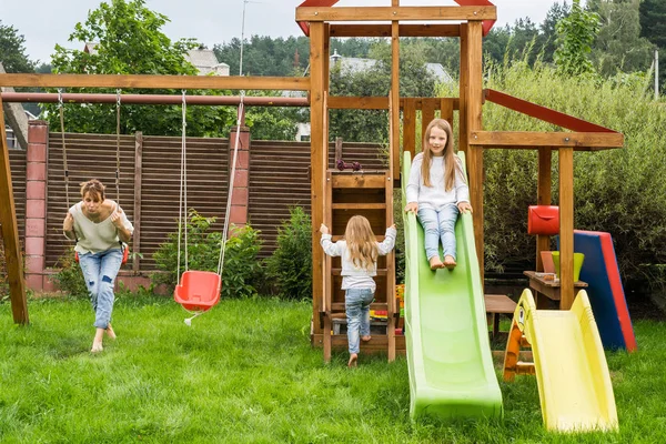 mother and daughters spends time on a swing and a children's slide. Mom with kids time together.