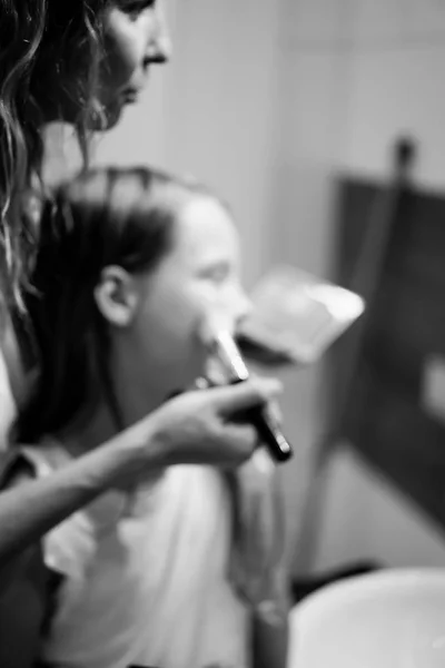 Mom and daughters do makeup in the bathroom, apply lipstick in front of the mirror. Mom and daughters have fun, spend time together.