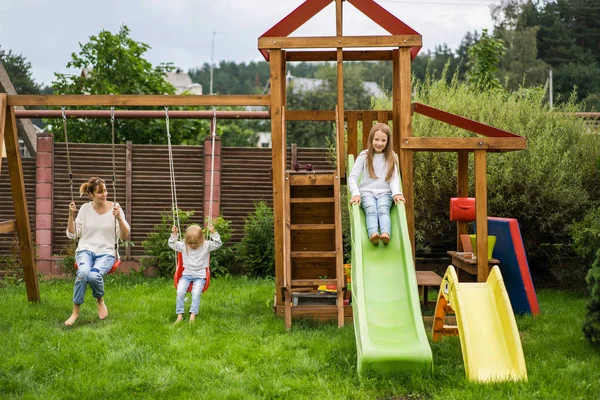 mother and daughters spends time on a swing and a children's slide. Mom with kids time together.