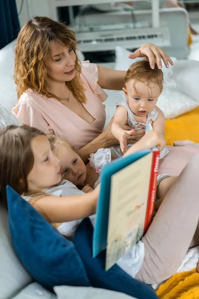 mother with three children reading a book in a homely atmosphere, sharing time with parents and children. mother, two daughters and a little son.