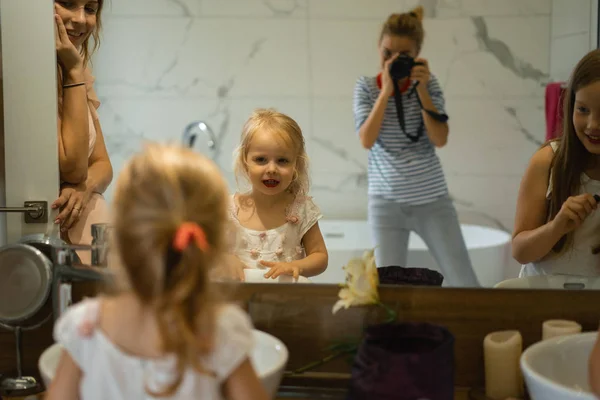 Mom and daughters do makeup in the bathroom, apply lipstick in front of the mirror. Mom and daughters have fun, spend time together.