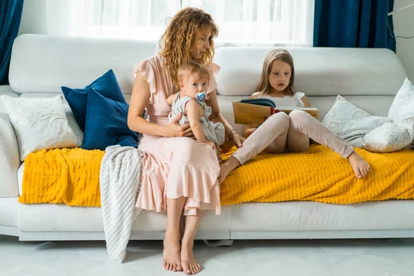 mother with three children reading a book in a homely atmosphere, sharing time with parents and children. mother, two daughters and a little son.