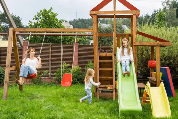 mother and daughters spends time on a swing and a children\'s slide. Mom with kids time together.