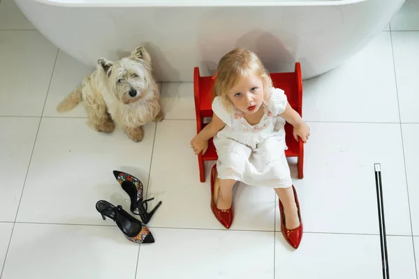 Mom and daughters do makeup in the bathroom, apply lipstick in front of the mirror. Daughters in her mother's heels. Mom and daughters have fun, spend time together.