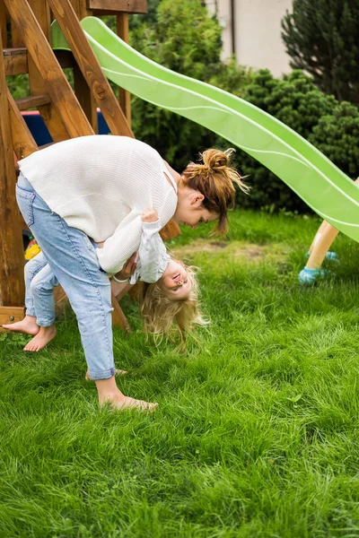 mother and daughters spends time on a swing and a children\'s slide. Mom with kids time together.