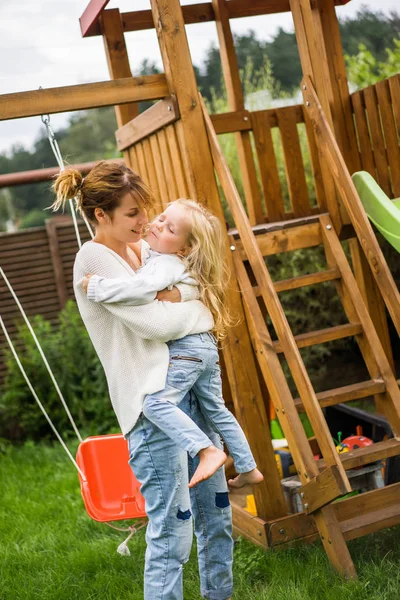 mother and daughters spends time on a swing and a children\'s slide. Mom with kids time together.
