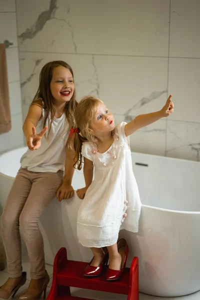 Mom and daughters do makeup in the bathroom, apply lipstick in front of the mirror. Daughters in her mother\'s heels. Mom and daughters have fun, spend time together.
