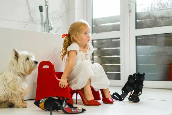 Mom and daughters do makeup in the bathroom, apply lipstick in front of the mirror. Daughters in her mother\'s heels. Mom and daughters have fun, spend time together.