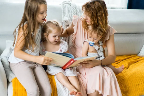 mother with three children reading a book in a homely atmosphere, sharing time with parents and children. mother, two daughters and a little son.