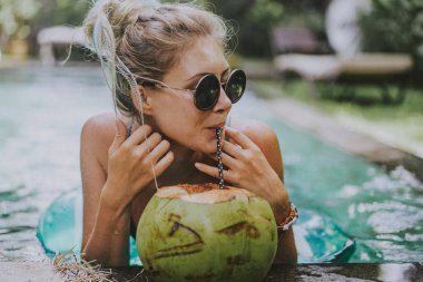 güzel genç kadın havuzda yüzüyor ve Hindistan cevizi içiyor. Tatilde erkek
