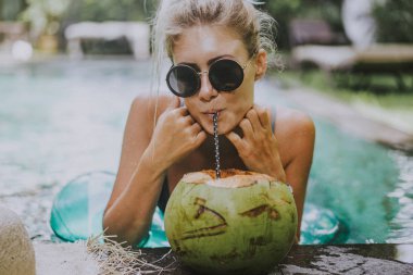 güzel genç kadın havuzda yüzüyor ve Hindistan cevizi içiyor. Tatilde erkek
