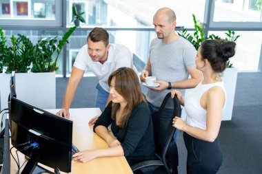 Tam konsantrasyon. Bir grup genç iş adamı arka planda iş arkadaşlarıyla ofis masasında otururken çalışıyor ve iletişim kuruyor.