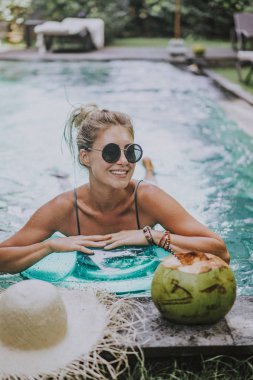 Yüzme havuzunda oturup dizüstü bilgisayarla çalışan çekici genç bir kadın..