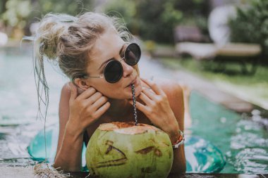 güzel genç kadın havuzda yüzüyor ve Hindistan cevizi içiyor. Tatilde erkek