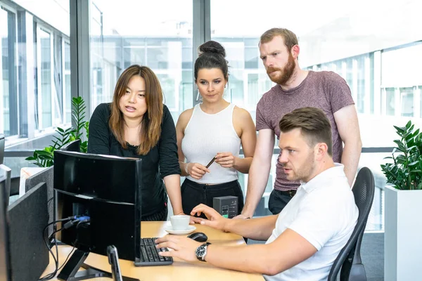 Full concentration at work. Group of young business people working and communicating while sitting at the office desk together with colleagues sitting in the background