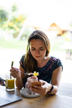 Dizüstü bilgisayarda çalışan genç bir kadın. Chia tohumları ve meyve suyuyla sağlıklı bir kahvaltı. Serbest bilgisayar akıllı telefon kahvaltısı. akıllı telefon ve laptop dokunmatik ekran görüntüsü kullanarak