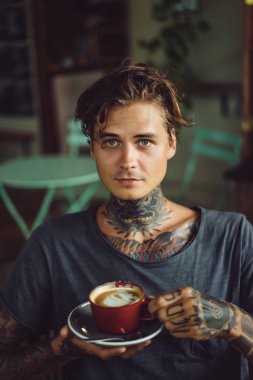 Yakışıklı dövmeli adam bir kafede kahvaltı yapıyor, kahve içiyor. dövmeler adam