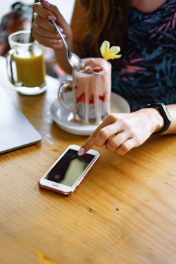 Dizüstü bilgisayarda çalışan genç bir kadın. Chia tohumları ve meyve suyuyla sağlıklı bir kahvaltı. Serbest bilgisayar akıllı telefon kahvaltısı. akıllı telefon ve laptop dokunmatik ekran görüntüsü kullanarak