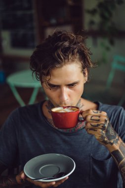 Yakışıklı dövmeli adam bir kafede kahvaltı yapıyor, kahve içiyor. dövmeler adam