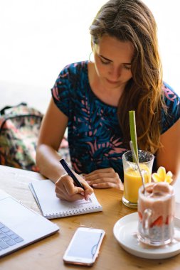 Dizüstü bilgisayarda çalışan genç bir kadın. Chia tohumları ve meyve suyuyla sağlıklı bir kahvaltı. Serbest bilgisayar akıllı telefon kahvaltısı. akıllı telefon ve laptop dokunmatik ekran görüntüsü kullanarak