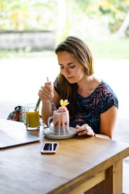 Dizüstü bilgisayarda çalışan genç bir kadın. Chia tohumları ve meyve suyuyla sağlıklı bir kahvaltı. Serbest bilgisayar akıllı telefon kahvaltısı. akıllı telefon ve laptop dokunmatik ekran görüntüsü kullanarak