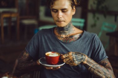 Yakışıklı dövmeli adam bir kafede kahvaltı yapıyor, kahve içiyor. dövmeler adam