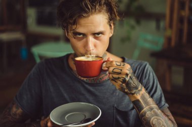 Yakışıklı dövmeli adam bir kafede kahvaltı yapıyor, kahve içiyor. dövmeler adam