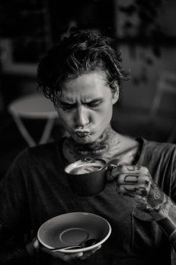 Yakışıklı dövmeli adam bir kafede kahvaltı yapıyor, kahve içiyor. dövmeler adam