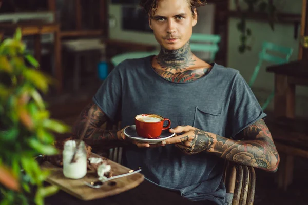 handsome tattooed man having breakfast in a cafe, drinking coffee. man in tattoos