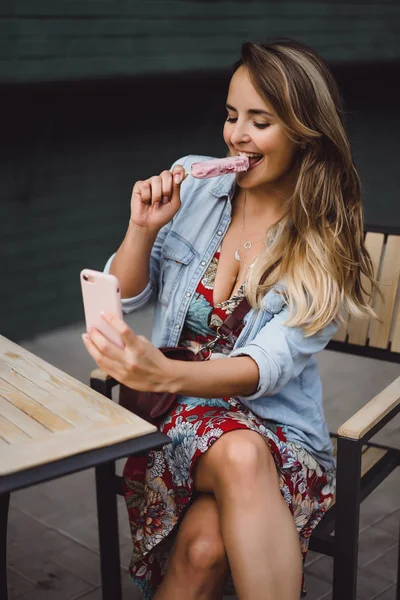 長い髪の美しい若い女性はアイスクリームを食べ スマートフォンで自分撮りをします 外のクローズアップポートレート — ストック写真