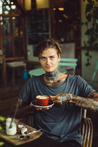 handsome tattooed man having breakfast in a cafe, drinking coffee. man in tattoos