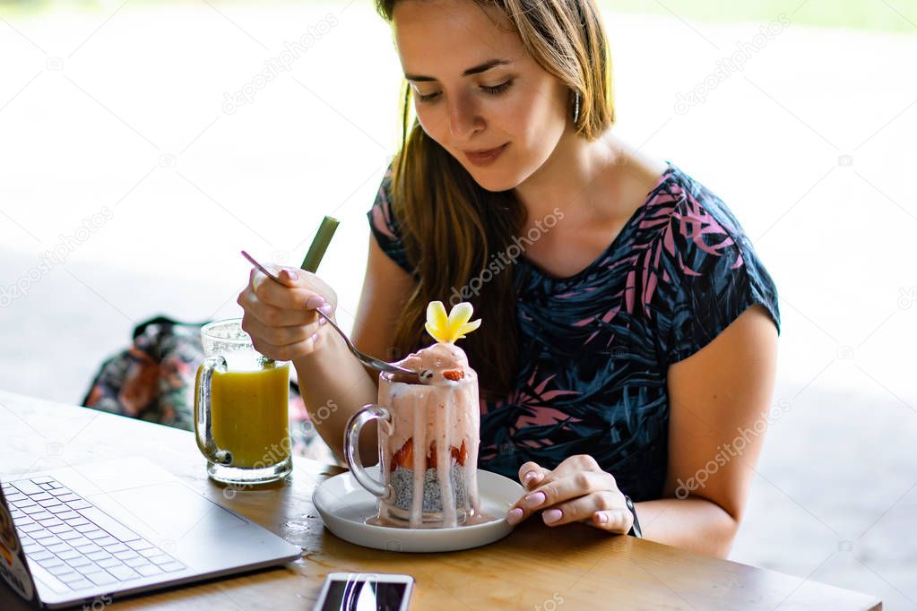 young female working on a laptop, healthy breakfast with chia seeds and juice. Freelance laptop smartphone breakfast. using smartphone and laptop touch screen display