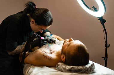 Dövme salonu süreci. Dövmeli bir kız dövme yaptırmış. Vücuduna dövme yapma işlemi için. Eller yakın plan..