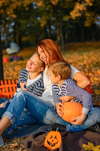 female with red hair with children. Mom with sons in the park on a picnic for Halloween.