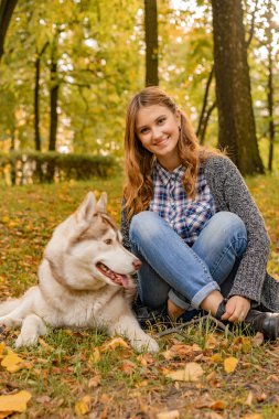 sonbahar parkında genç kadın bir husky köpek ile yürüyor.