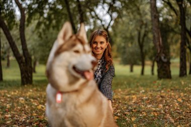 sonbahar parkında genç kadın bir husky köpek ile yürüyor.