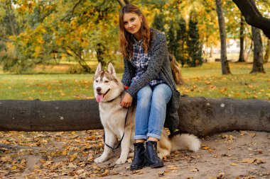 sonbahar parkında genç kadın bir husky köpek ile yürüyor.
