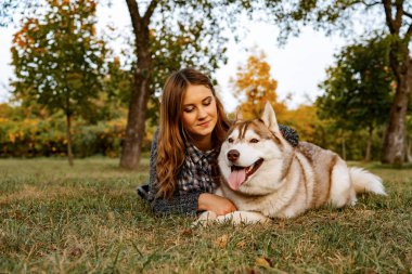 sonbahar parkında genç kadın bir husky köpek ile yürüyor.