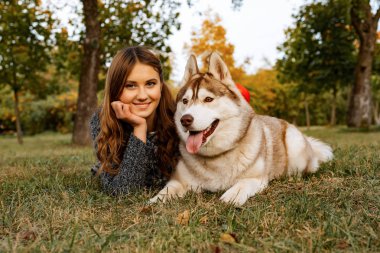 sonbahar parkında genç kadın bir husky köpek ile yürüyor.