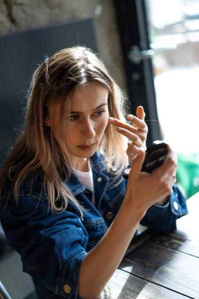 Joven hermosa mujer en un café se mira en el espejo se endereza — Foto de Stock