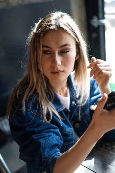 Young beautiful woman in a cafe looks in the mirror straightens — Stock Photo, Image