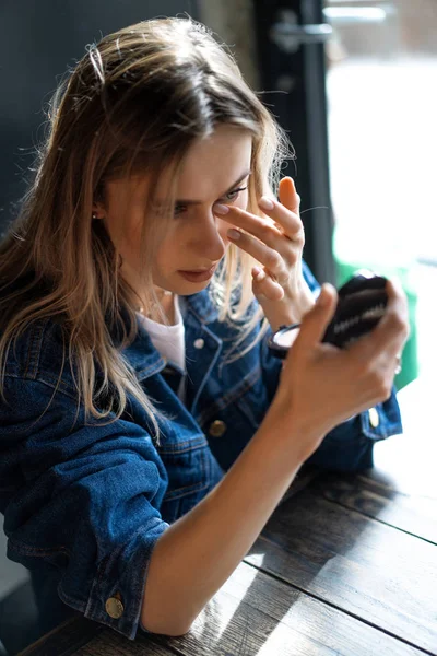 Giovane bella donna in un caffè si guarda allo specchio raddrizza — Foto Stock