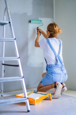 Genç ve güzel bir kadın dairede tamirat yapıyor, duvarları silindirle boyuyor. Molar çalışması.