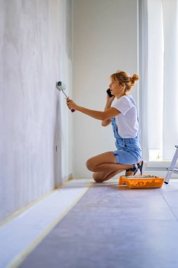 Genç ve güzel bir kadın dairede tamirat yapıyor, duvarları silindirle boyuyor. Molar çalışması.