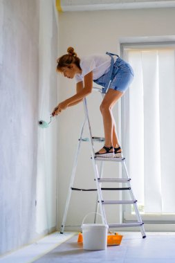 Genç ve güzel bir kadın dairede tamirat yapıyor, duvarları silindirle boyuyor. Molar çalışması.