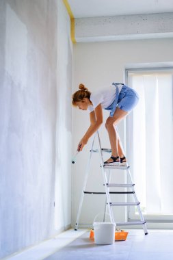 Genç ve güzel bir kadın dairede tamirat yapıyor, duvarları silindirle boyuyor. Molar çalışması.