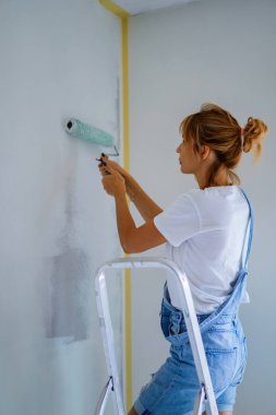 Genç ve güzel bir kadın dairede tamirat yapıyor, duvarları silindirle boyuyor. Molar çalışması.