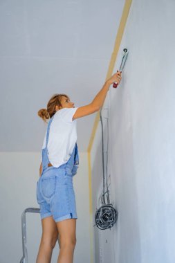 Genç ve güzel bir kadın dairede tamirat yapıyor, duvarları silindirle boyuyor. Molar çalışması.