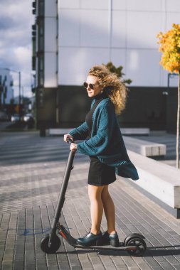İşe elektrikli scooterla giden genç, güzel bir kadın, modern kız, yeni nesil, elektrik nakli, ekolojik ulaşım, ekolojik ulaşım, gün batımı