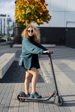 İşe elektrikli scooterla giden genç, güzel bir kadın, modern kız, yeni nesil, elektrik nakli, ekolojik ulaşım, ekolojik ulaşım, gün batımı